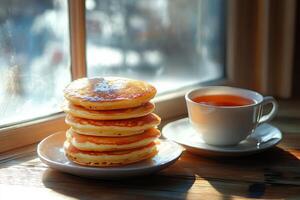 A stack of pancakes on a plate next to a cup of tea photo