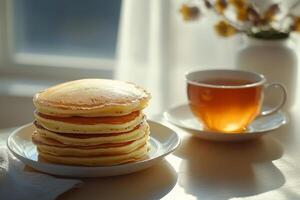 A stack of pancakes on a plate next to a cup of tea photo