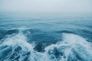 Waves crashing against each other in a tranquil blue ocean on a foggy day photo