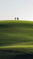 Three people standing on a hill in a green field photo