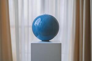 A blue glass ball sits on a pedestal in front of curtains photo