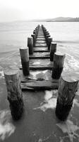 Black and white photograph of a pier on the beach photo