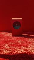 A red speaker sits on a carpet in front of a wall photo