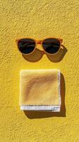 A pair of sunglasses and a towel on a yellow wall photo
