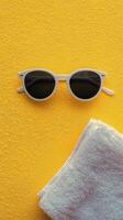 A pair of sunglasses and a towel on a yellow background photo