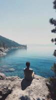 A person sitting on a rock overlooking a lake photo