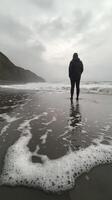 A person standing on the beach looking at the ocean photo