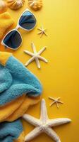 Summer vacation concept with beach towel, sunglasses and starfish on yellow background photo