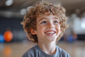 A young boy with curly hair smiles while standing in a gym photo