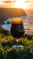 A glass of beer sitting on the grass near the ocean photo