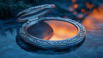 A silver compact mirror on a table with a sunset in the background photo