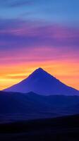 A mountain is silhouetted against a colorful sunset photo