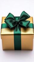 Gift box wrapped in gold with a dark green ribbon and bow on a light surface photo