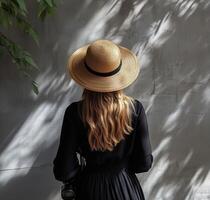 Woman with straw hat standing against a textured wall in soft sunlight photo
