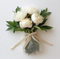 Elegant bouquet of white peonies wrapped in burlap with a ribbon decoration at a bright backdrop photo