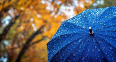 Bright blue umbrella caught in rain with autumn foliage in the background during a rainy day photo