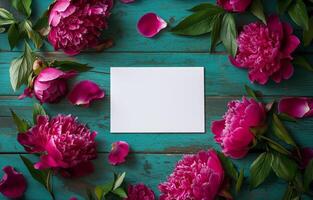 Vibrant peonies with petals arranged around a blank white card on a rustic wooden table photo