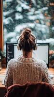 Woman wearing headphones working on computer in front of window photo