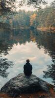 Person meditating by a peaceful lake surrounded by mountains and mist during early morning hours photo