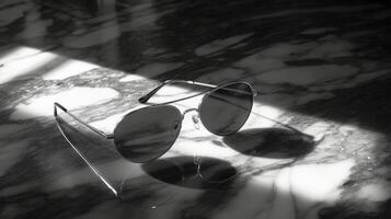 Reflective sunglasses resting on marble surface with shadows cast by sunlight photo