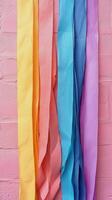 A rainbow of colored paper streamers against a pink wall photo
