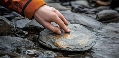 A hand gently touches a smooth rock in a stream photo