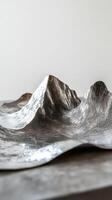 Silver mountain range sculpture displayed against a minimalist background photo