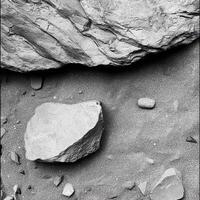 Rocks and pebbles sit on fine sand in monochrome photo