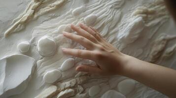 Hand touches tactile artwork featuring white stones and textures photo