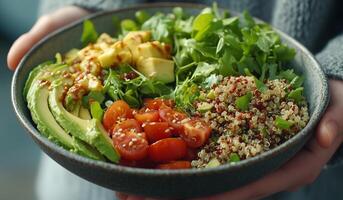 A person holding a bowl of salad with avocado, tomatoes, and quinoa photo