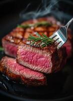 Grilled steak with rosemary and fork on black plate photo