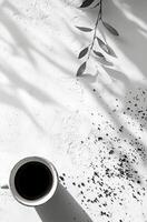 Dark coffee cup placed on a textured white surface next to scattered coffee grounds and green leaf photo