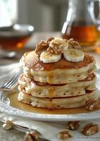 Stack of fluffy pancakes topped with bananas and walnuts served with syrup photo