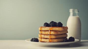 Stacked pancakes with blackberries and honey served with a glass of milk photo