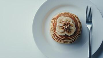 Delicious stack of pancakes topped with banana and nuts on a white plate photo