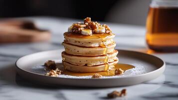 Fluffy pancakes stacked high with syrup and nuts on a marble table in a cozy setting photo