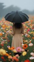 Woman with black umbrella walks through colorful flower field on a misty day photo