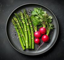 Fresh asparagus and radishes served on a black plate with seasoning and garnish photo
