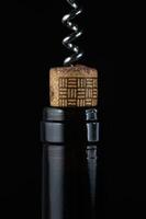 Corkscrew twisting in a bottle of dark liquid against a black background photo