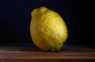 Bright lemon resting on a wooden surface against a dark backdrop under soft light photo