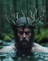 A man with a beard and a crown of branches stands in a body of water photo