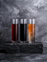Three different colored drinks in tall glasses on a stone photo