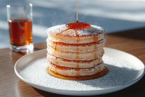 Stack of pancakes with powdered sugar and maple syrup being poured on top photo