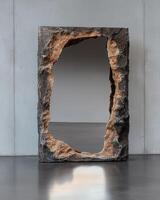 A unique mirror with a rough stone frame stands on a reflective floor photo