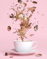 Golden liquid splashing into a white teacup on a pink background photo