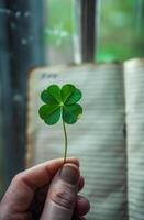 A person is holding a green leaf in their hand, which is a symbol of good luck. The leaf is placed on top of a book, which is open to a page with writing on it photo