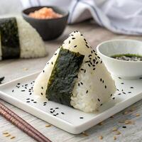 A triangular rice ball with a strip of nori at the base, displayed upright and sprinkled with black sesame seeds photo
