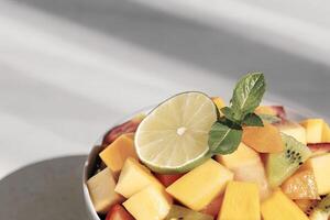 A tropical fruit salad with a slice of lime and mint leaves photo