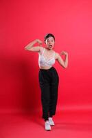 A woman in a sports bra and black pants is flexing her arms while standing with her mouth open. isolated on a red background photo