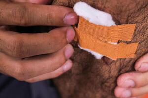 A close up of a person applying a bandage to a wound on their skin. The person is using their fingers to press the bandage into place. photo